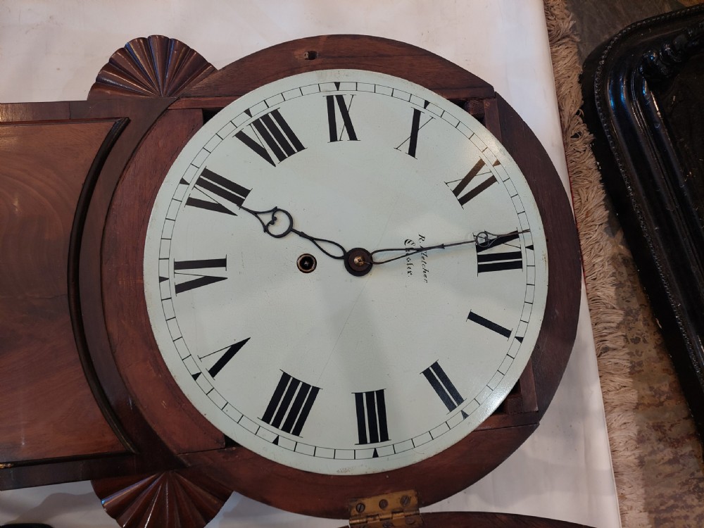 A George III mahogany drop dial wall clock featuring a white circular dial with Roman numerals above a flame mahogany trunk door. View IX