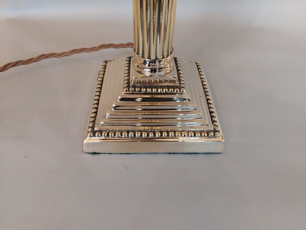 An early twentieth-century brass table lamp featuring a fluted Corinthian column shaft on a stepped pedestal base, topped with a patterned fabric shade with tassel and bead fringe. View II