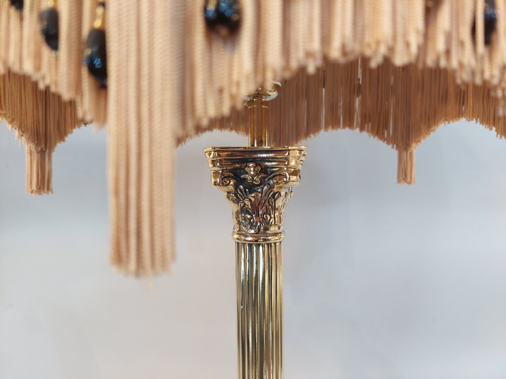 An early twentieth-century brass table lamp featuring a fluted Corinthian column shaft on a stepped pedestal base, topped with a patterned fabric shade with tassel and bead fringe. View III