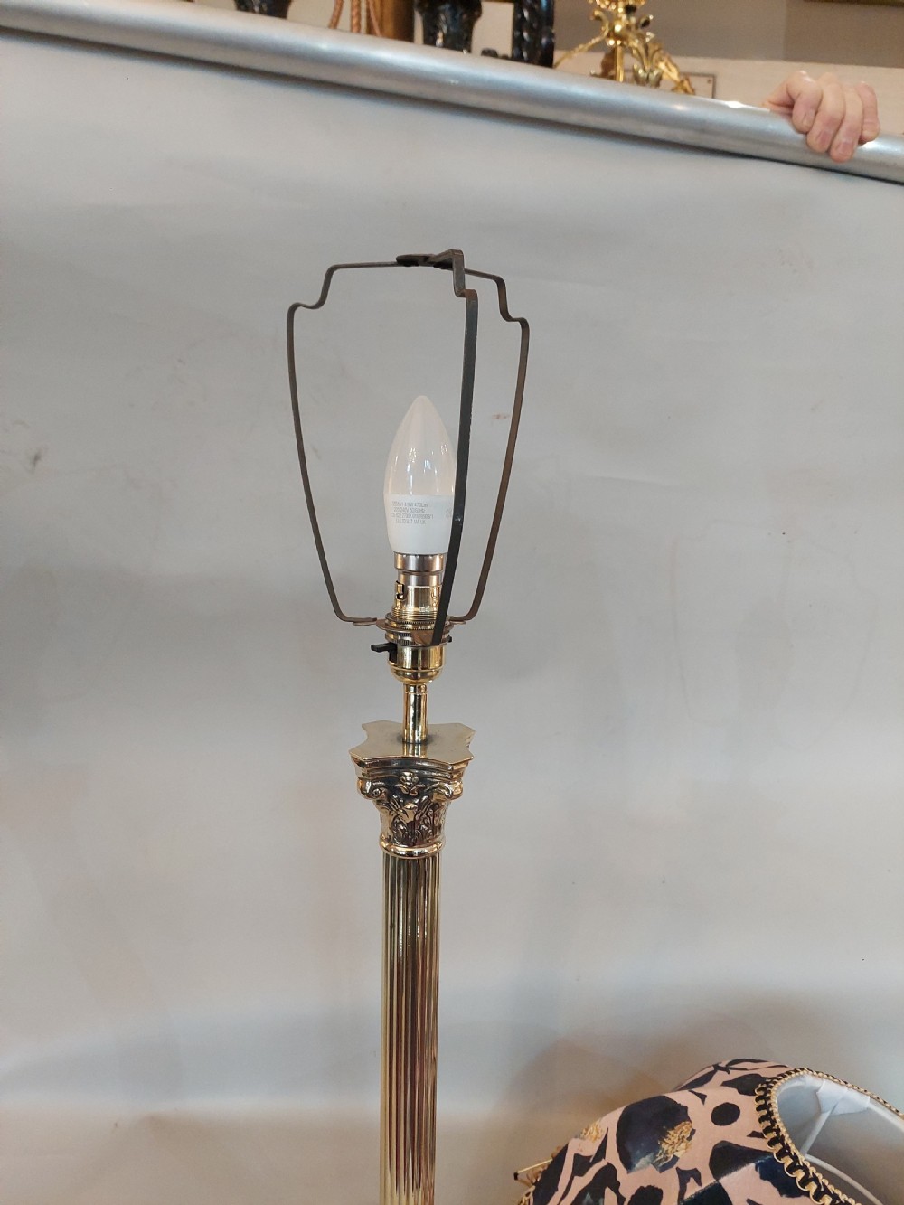 An early twentieth-century brass table lamp featuring a fluted Corinthian column shaft on a stepped pedestal base, topped with a patterned fabric shade with tassel and bead fringe. View V
