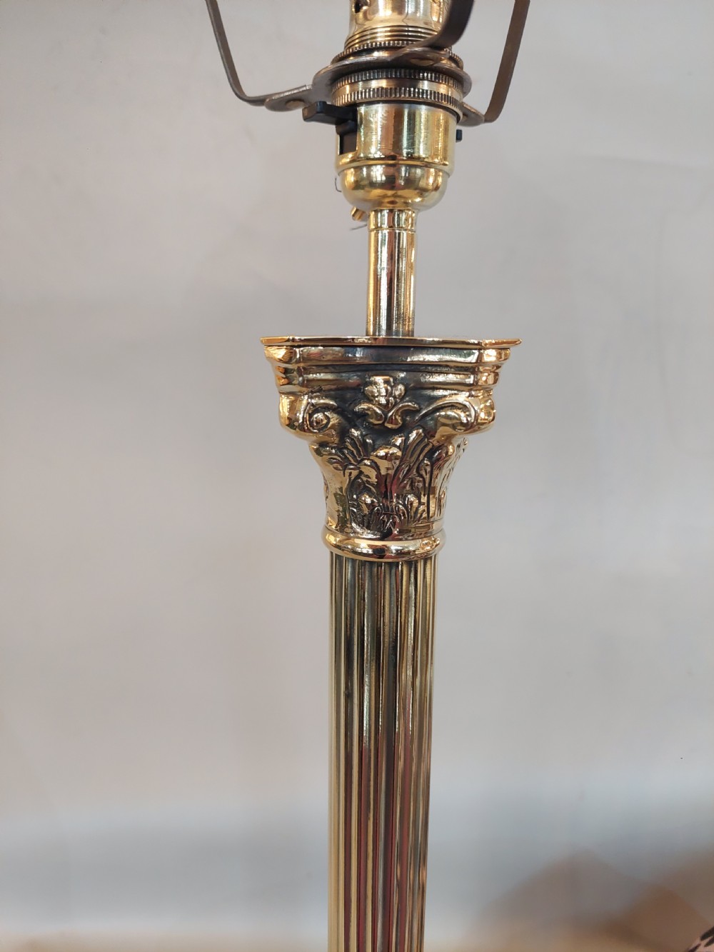 An early twentieth-century brass table lamp featuring a fluted Corinthian column shaft on a stepped pedestal base, topped with a patterned fabric shade with tassel and bead fringe. View VI