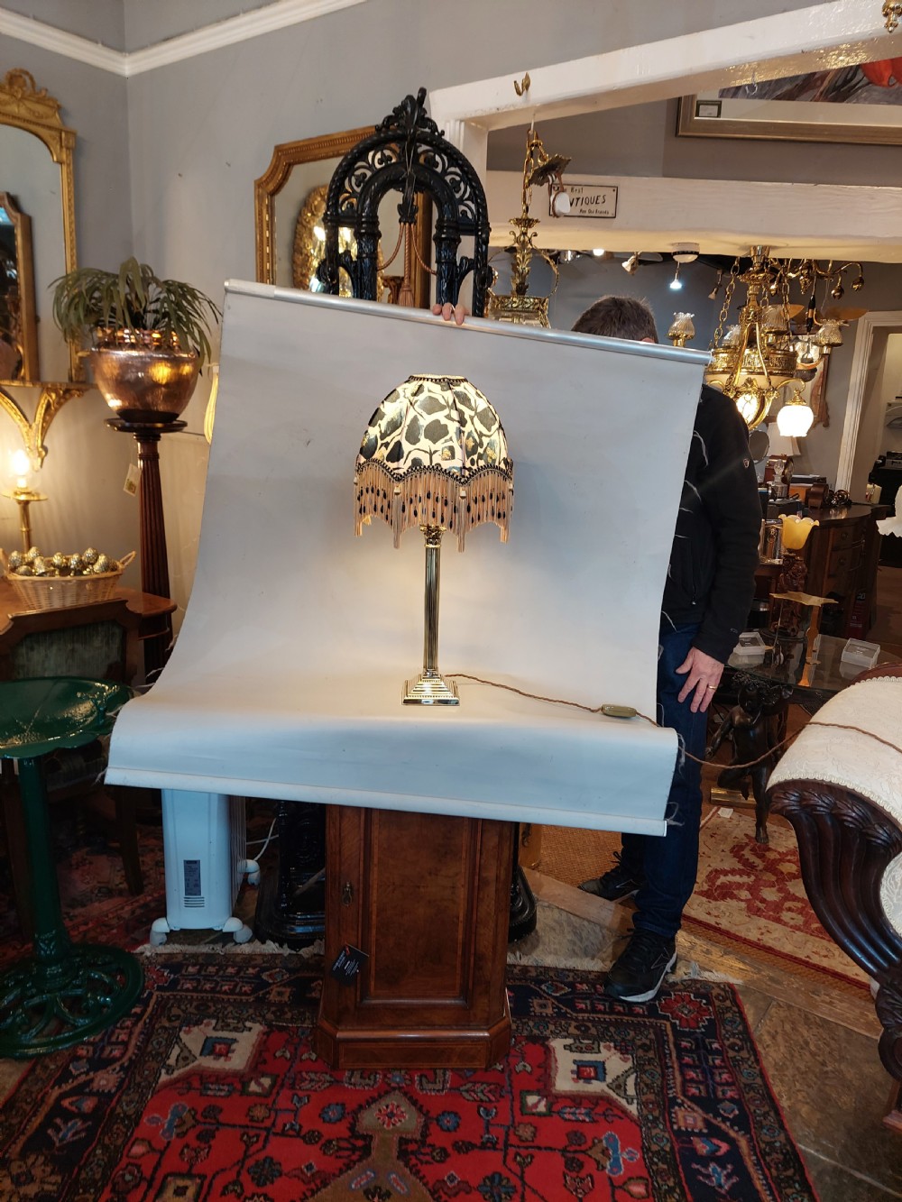 An early twentieth-century brass table lamp featuring a fluted Corinthian column shaft on a stepped pedestal base, topped with a patterned fabric shade with tassel and bead fringe. View VII