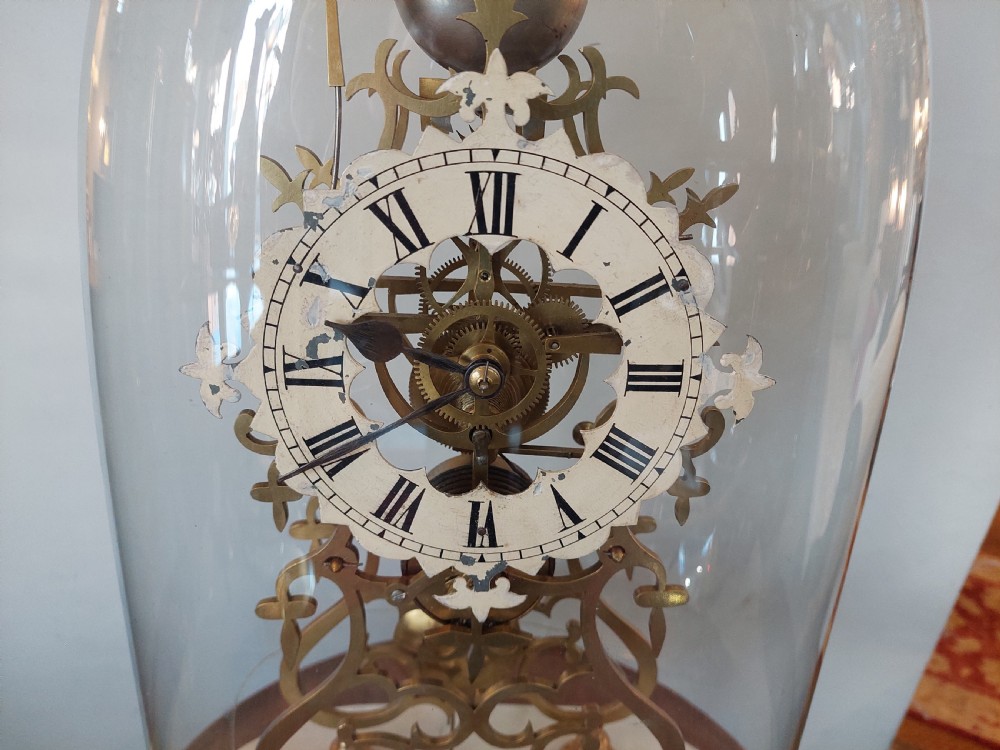 A Victorian brass skeleton clock with openwork gear movement, silvered chapter ring, and top bell, enclosed under a clear glass dome on a white marble base. View II