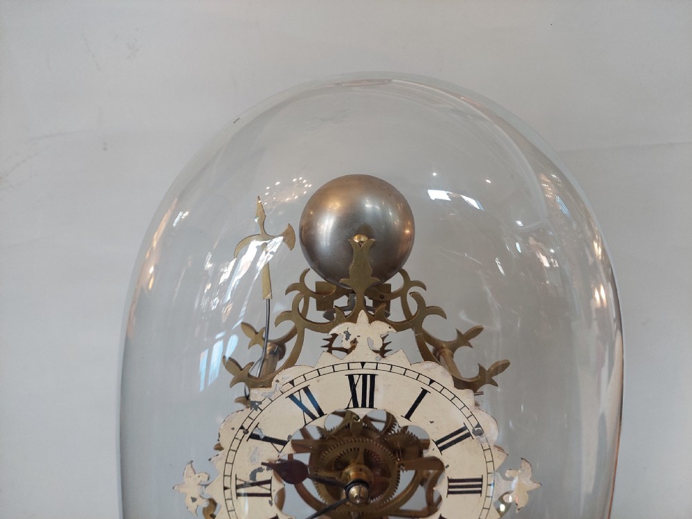 A Victorian brass skeleton clock with openwork gear movement, silvered chapter ring, and top bell, enclosed under a clear glass dome on a white marble base. View III