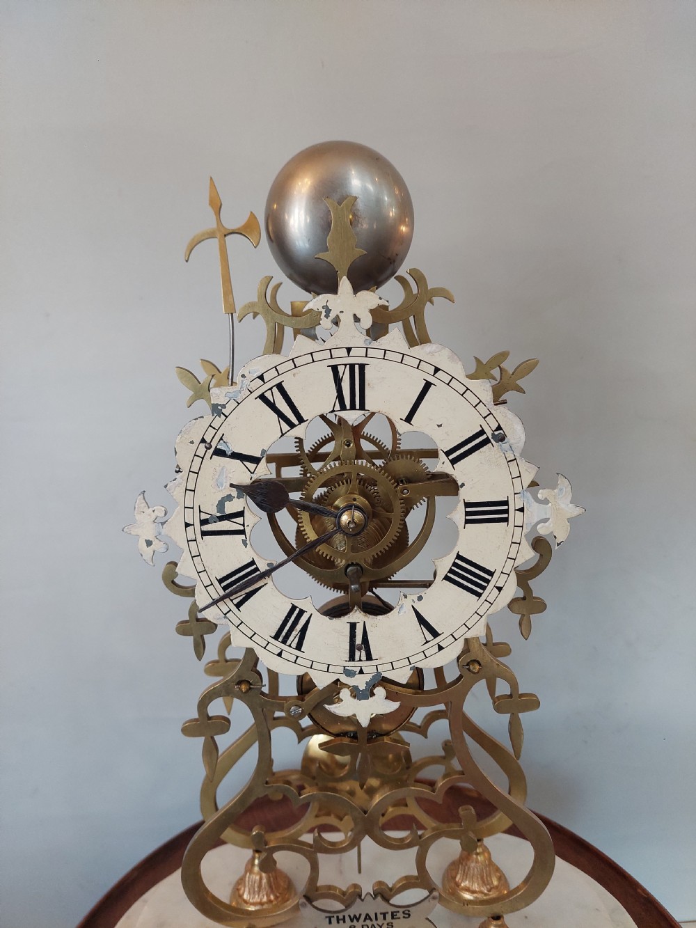 A Victorian brass skeleton clock with openwork gear movement, silvered chapter ring, and top bell, enclosed under a clear glass dome on a white marble base. View V
