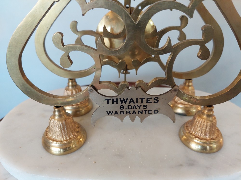 A Victorian brass skeleton clock with openwork gear movement, silvered chapter ring, and top bell, enclosed under a clear glass dome on a white marble base. View VI