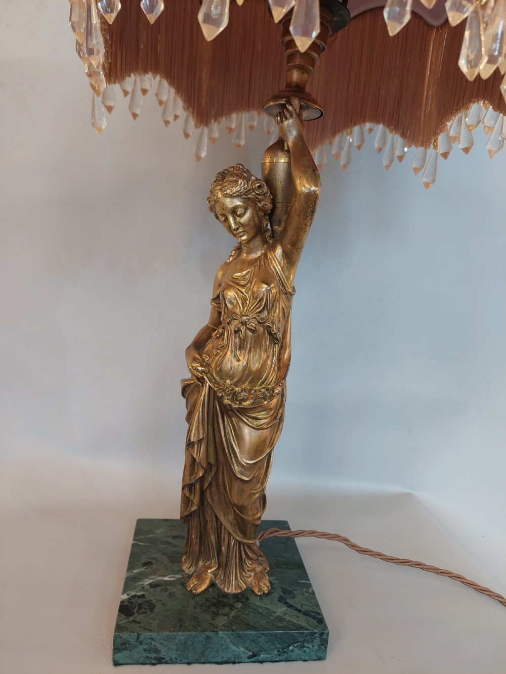 An antique Victorian cold-painted bronze table lamp shaped as a classical standing female figure on a green marble base, topped with a pink silk fringed shade. View IV