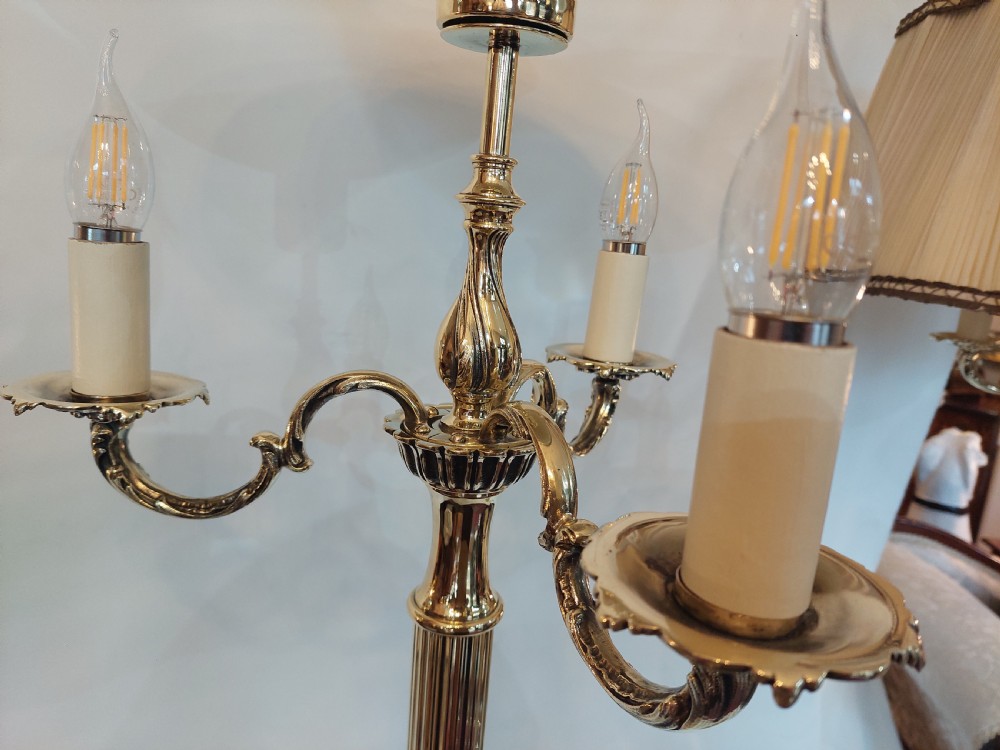 A pair of 1920s polished brass standard floor lamps featuring reeded columns, decorative cast bases, and pleated fabric shades. View VI