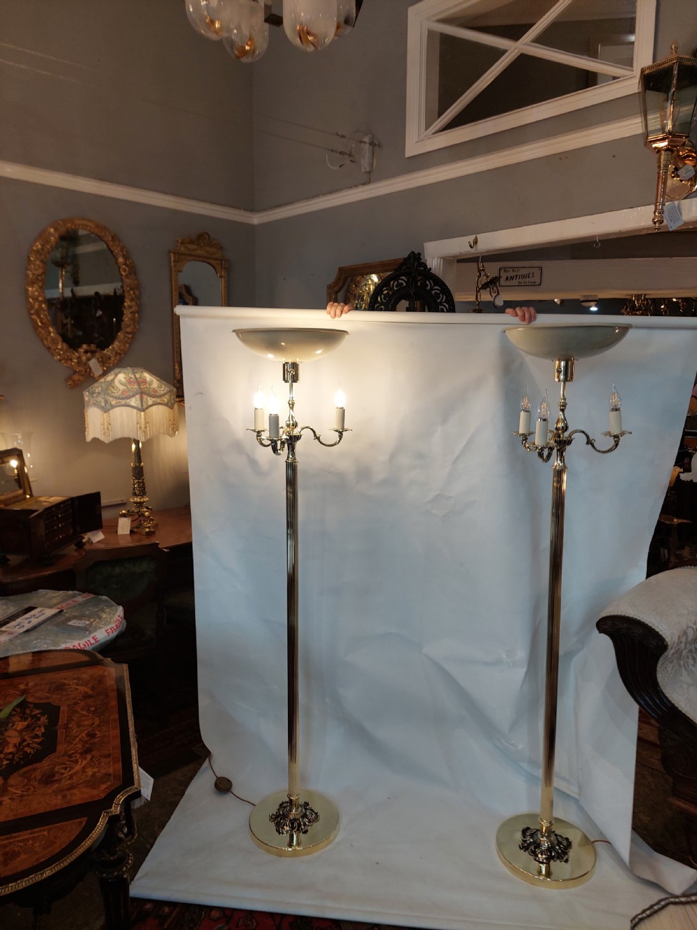 A pair of 1920s polished brass standard floor lamps featuring reeded columns, decorative cast bases, and pleated fabric shades. View XII