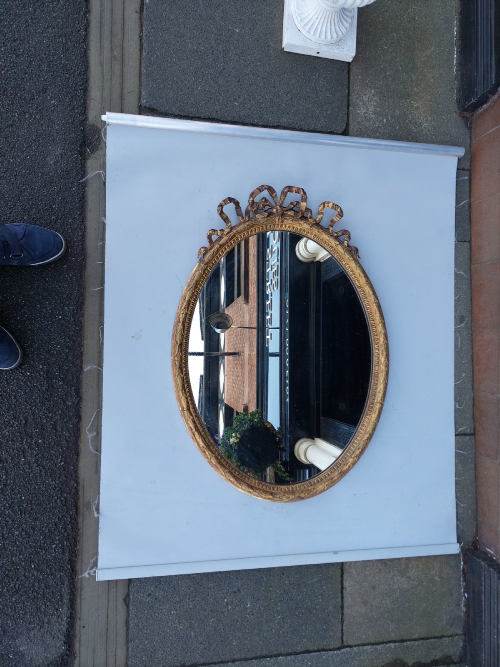A mid 19th-century oval wall mirror featuring a giltwood frame topped with a carved ribbon bow cresting. View II