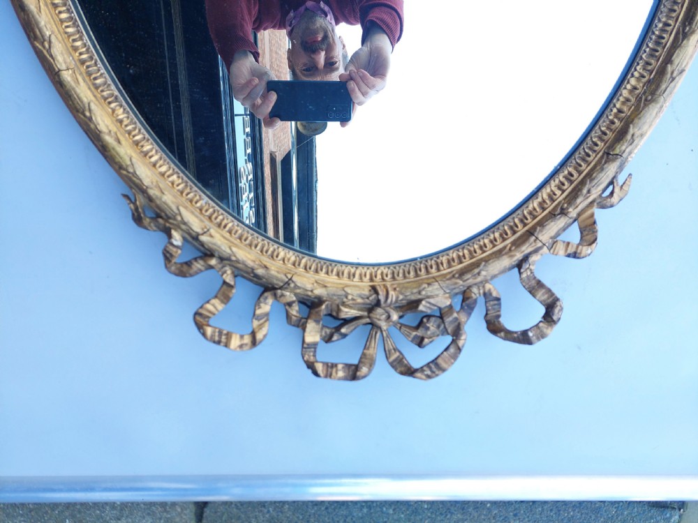 A mid 19th-century oval wall mirror featuring a giltwood frame topped with a carved ribbon bow cresting. View III