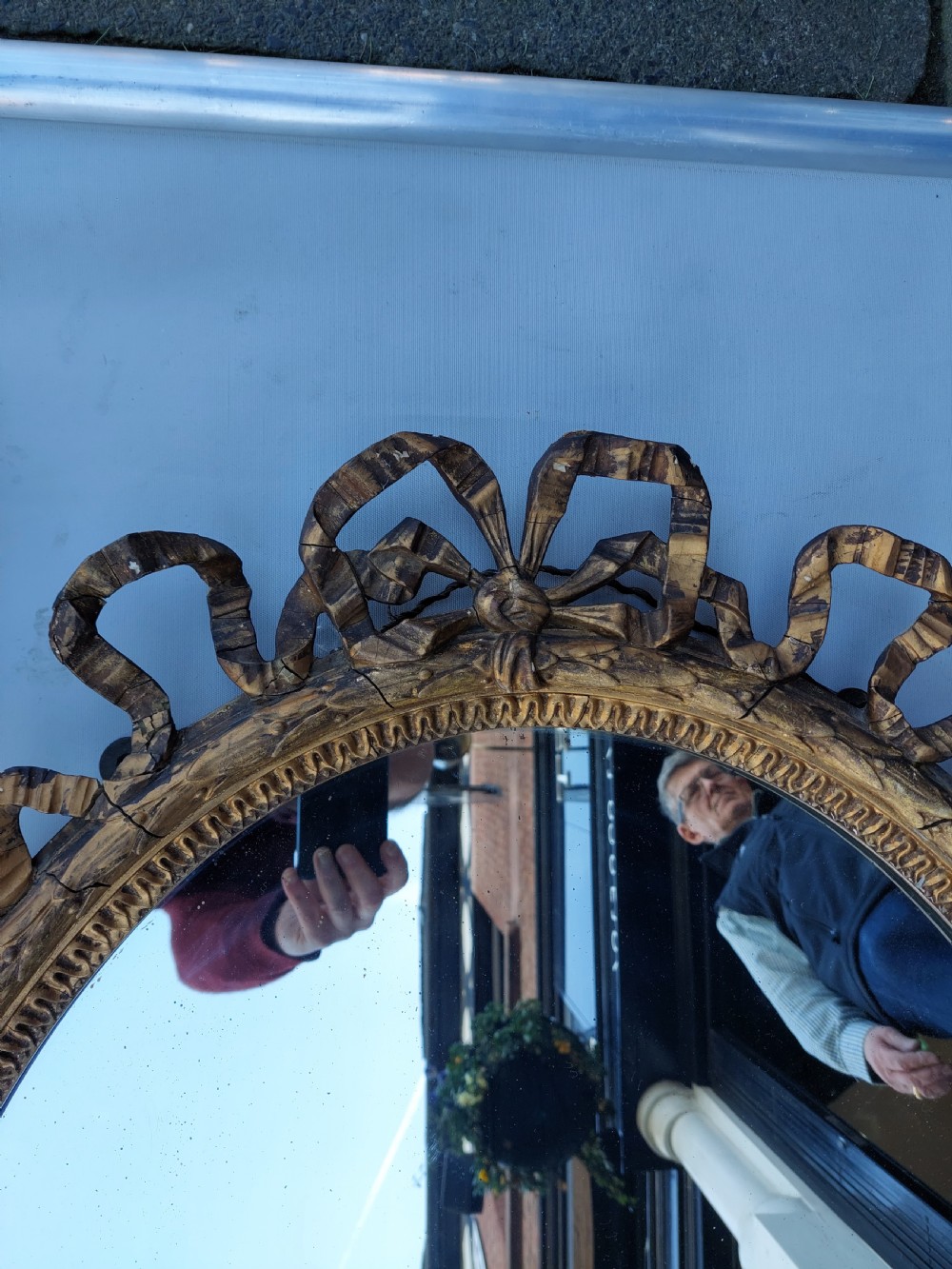 A mid 19th-century oval wall mirror featuring a giltwood frame topped with a carved ribbon bow cresting. View VII