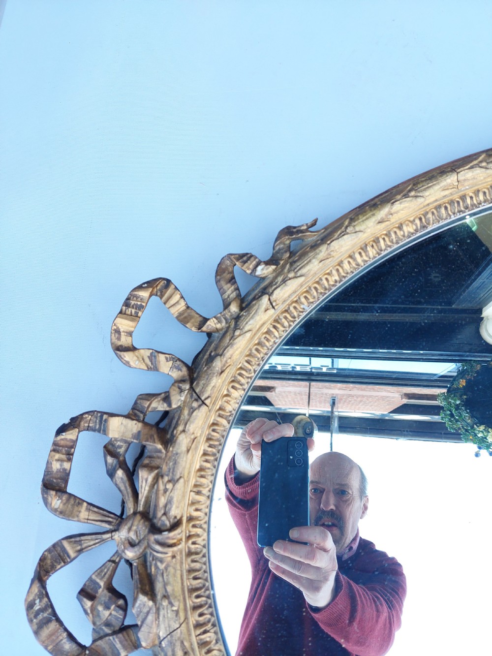 A mid 19th-century oval wall mirror featuring a giltwood frame topped with a carved ribbon bow cresting. View VIII