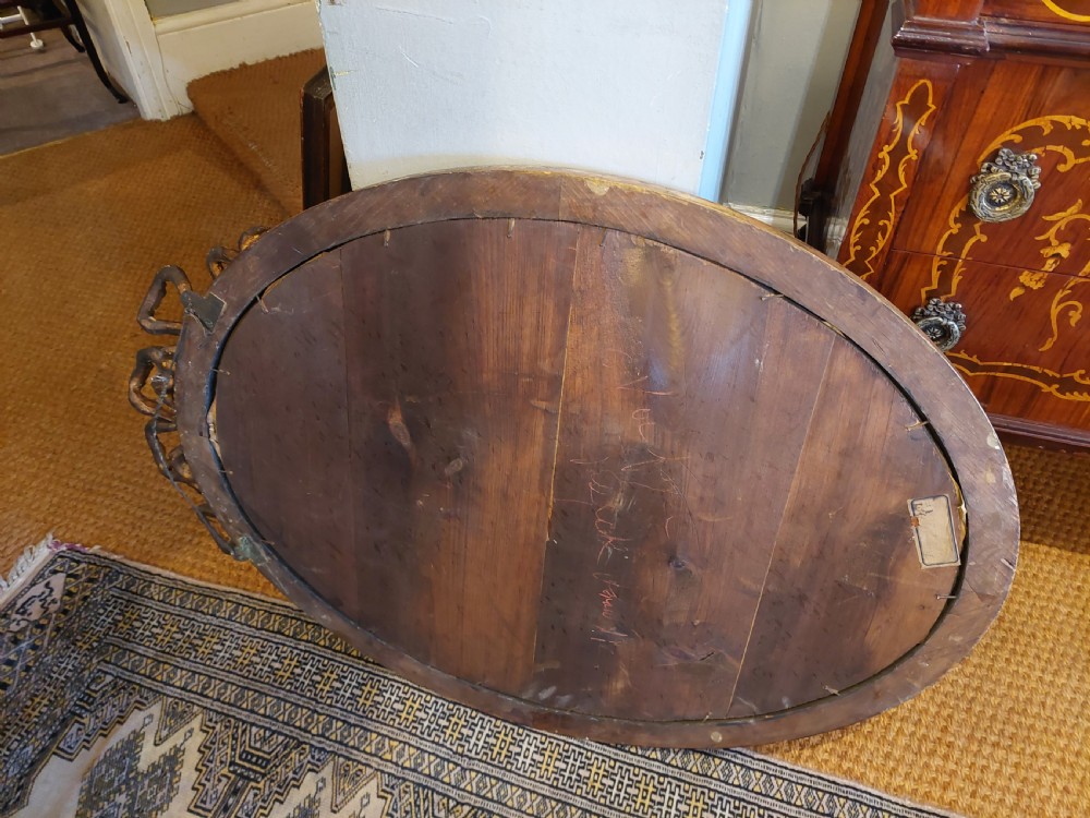 A mid 19th-century oval wall mirror featuring a giltwood frame topped with a carved ribbon bow cresting. View X