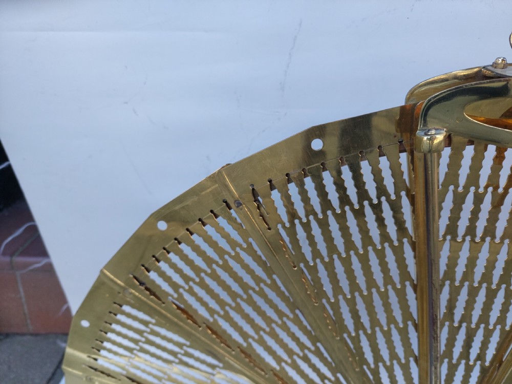 A Victorian folding brass fireplace screen shaped like an open fan with pierced filigree blades mounted on a cast base. View III