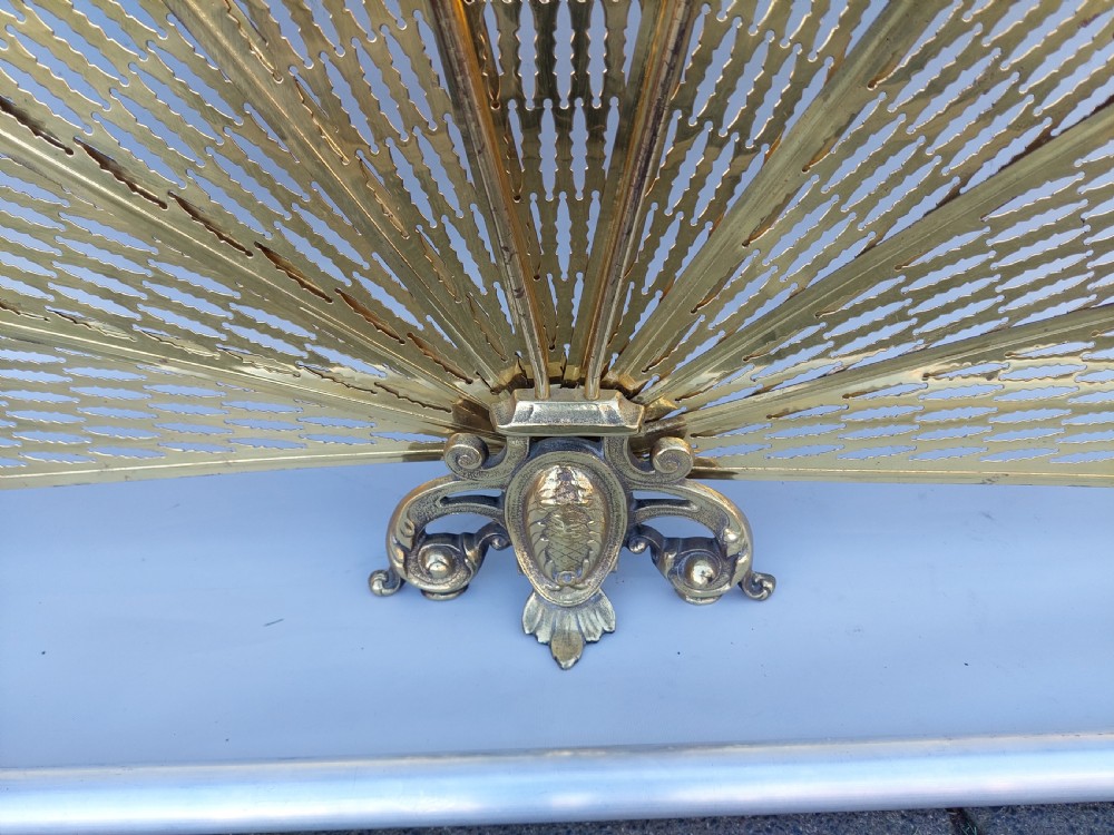 A Victorian folding brass fireplace screen shaped like an open fan with pierced filigree blades mounted on a cast base. View IV