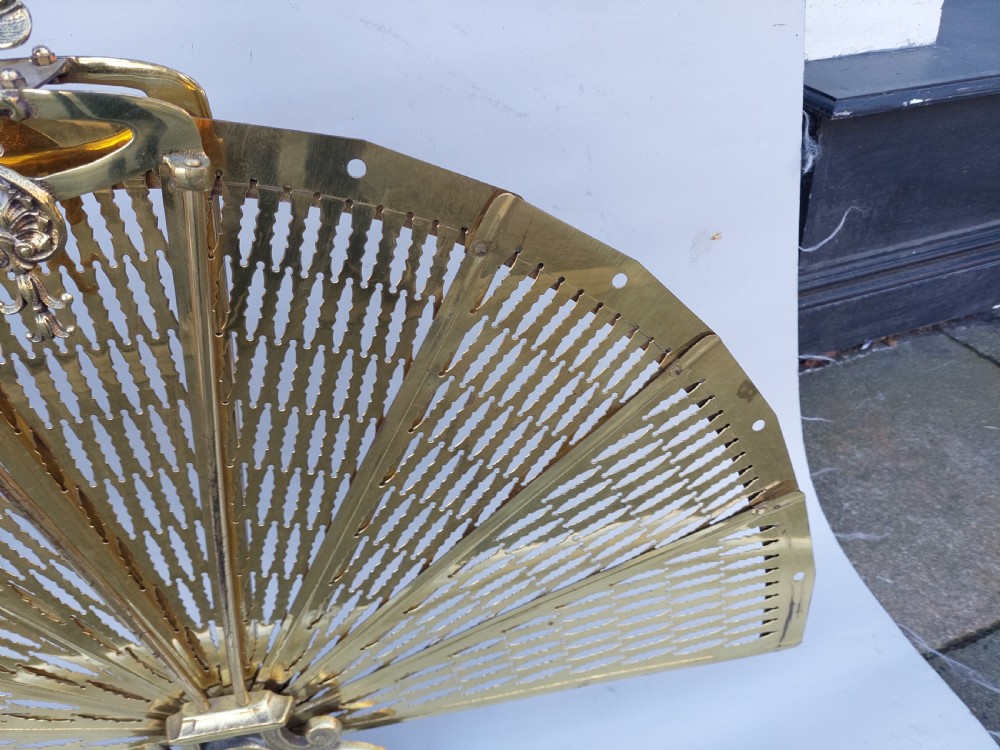 A Victorian folding brass fireplace screen shaped like an open fan with pierced filigree blades mounted on a cast base. View V
