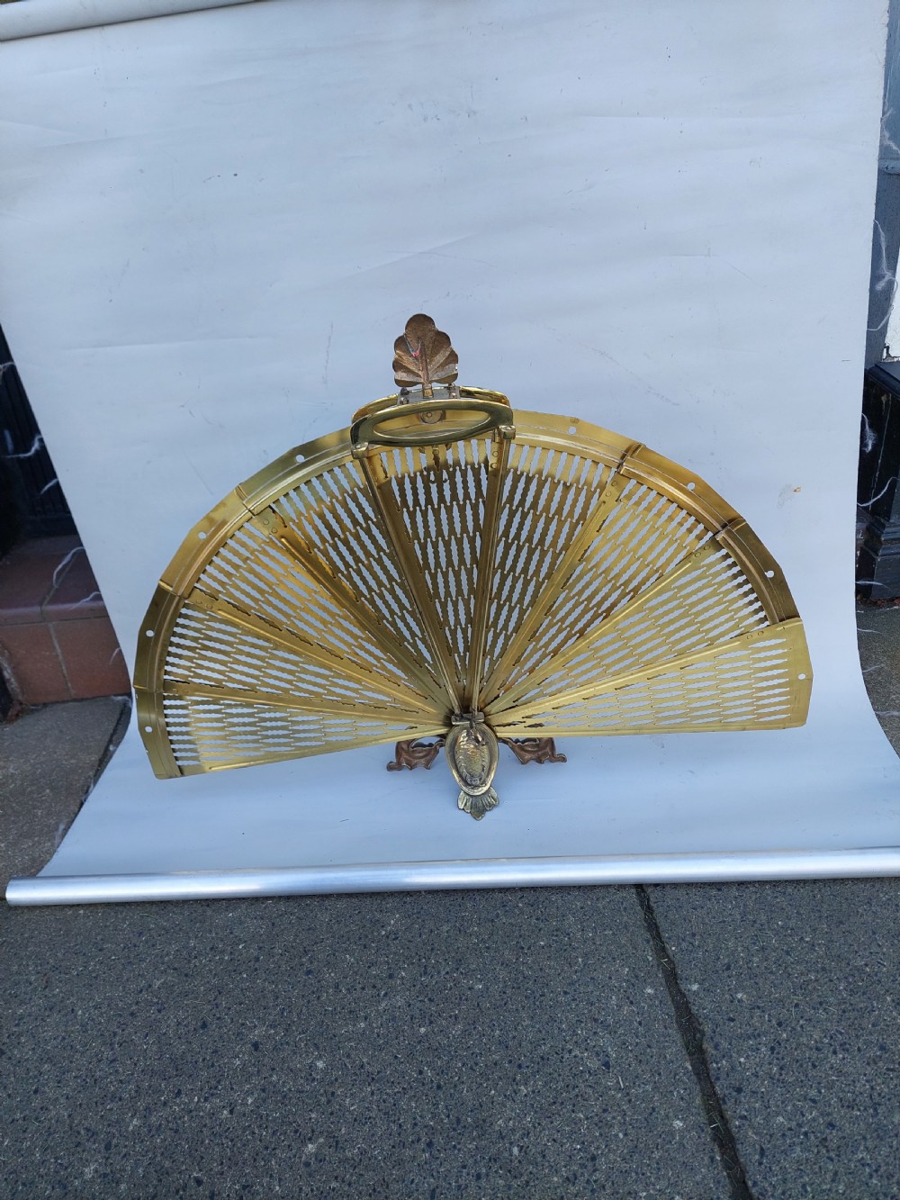 A Victorian folding brass fireplace screen shaped like an open fan with pierced filigree blades mounted on a cast base. View VII