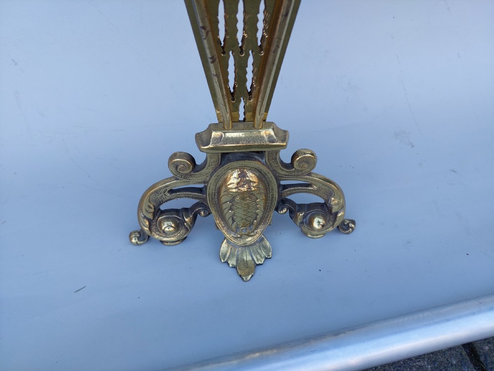 A Victorian folding brass fireplace screen shaped like an open fan with pierced filigree blades mounted on a cast base. View VIII