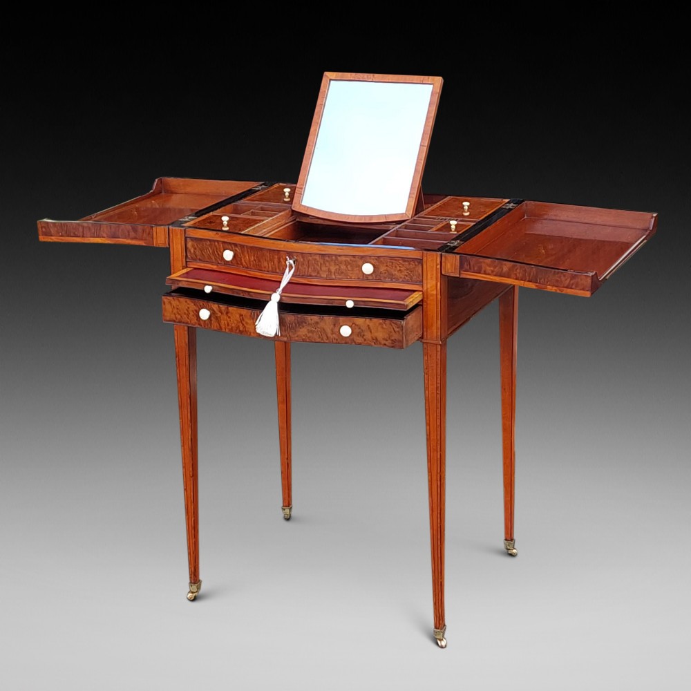A George III satinwood and mahogany gentlemans wash stand with extended hinged top flaps, an upright central mirror, and tapered inlaid legs on brass castors.