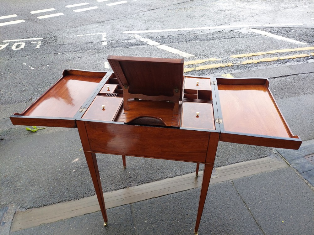 A George III satinwood and mahogany gentlemans wash stand with extended hinged top flaps, an upright central mirror, and tapered inlaid legs on brass castors. View V