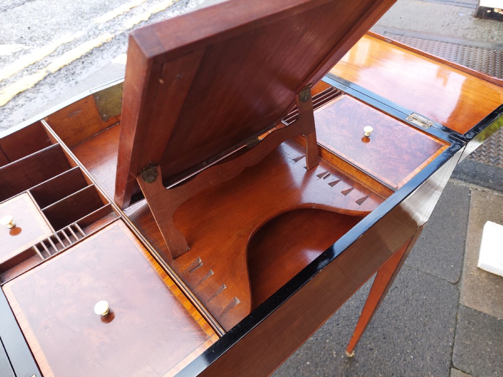 A George III satinwood and mahogany gentlemans wash stand with extended hinged top flaps, an upright central mirror, and tapered inlaid legs on brass castors. View VII