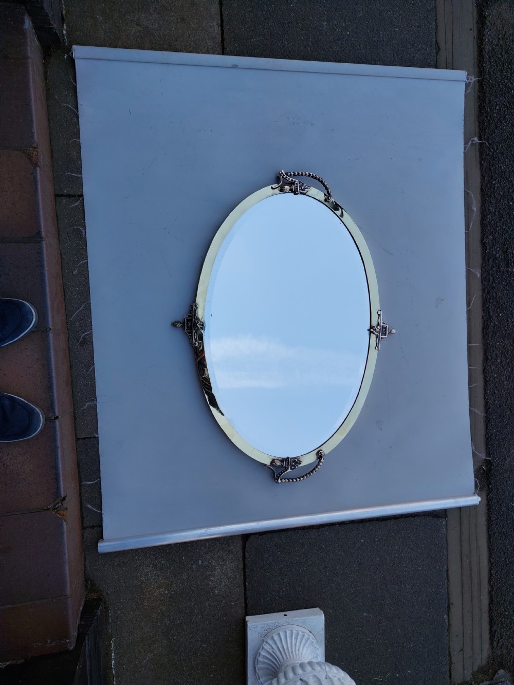 An early 20th-century oval wall mirror featuring a pale glass border anchored by four ornate metal mounts at the top, bottom, and sides. View II