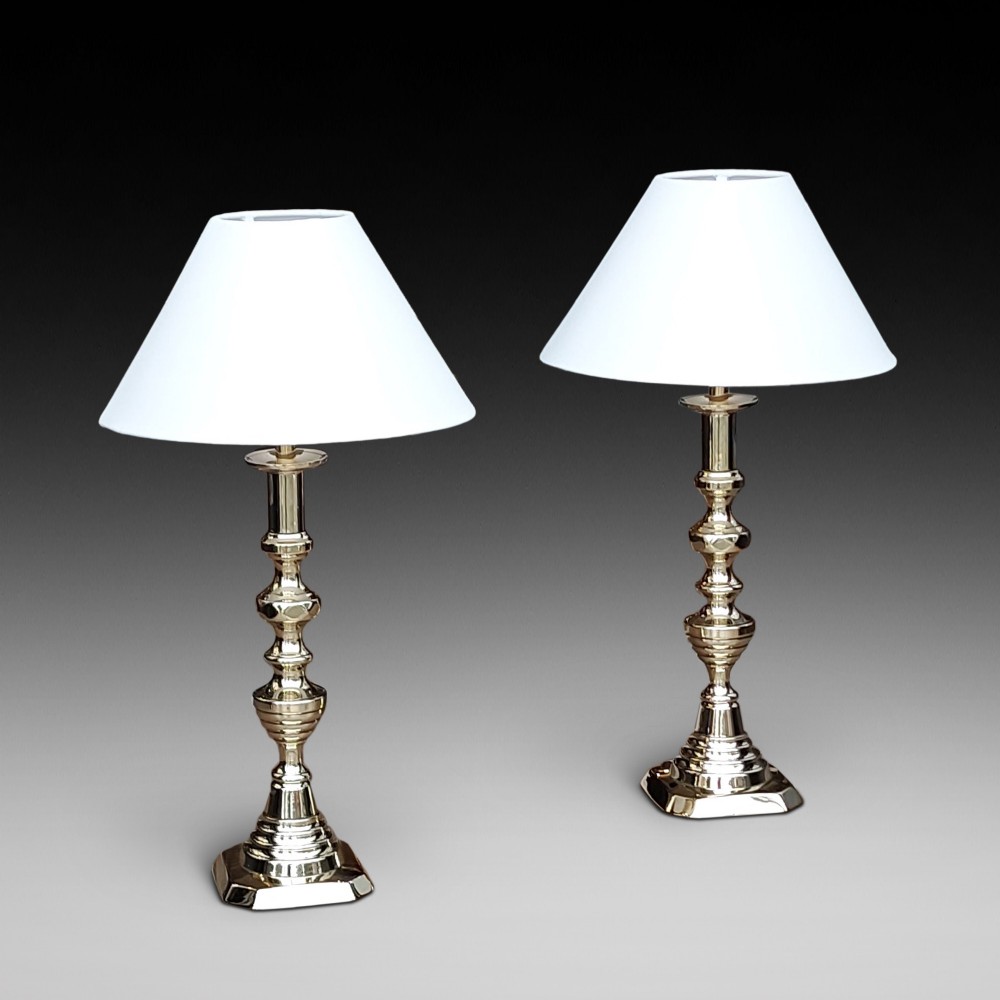 A pair of turned Victorian-style polished brass table lamps fitted with white conical lampshades.