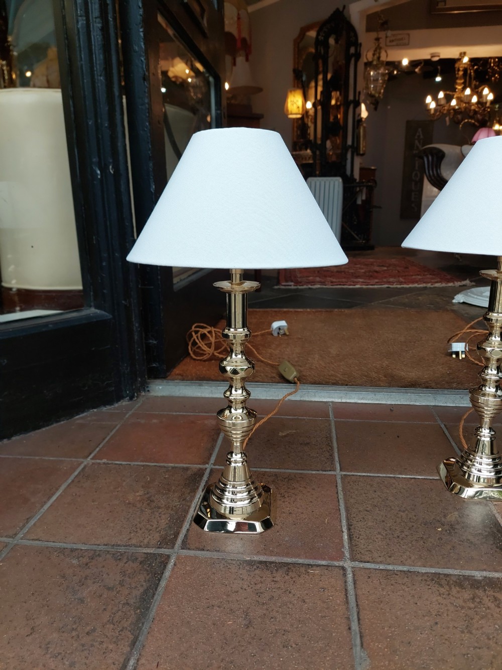 A pair of turned Victorian-style polished brass table lamps fitted with white conical lampshades. View II