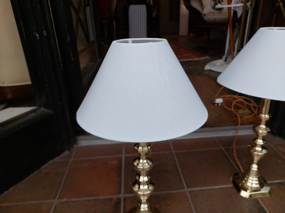 A pair of turned Victorian-style polished brass table lamps fitted with white conical lampshades. View V