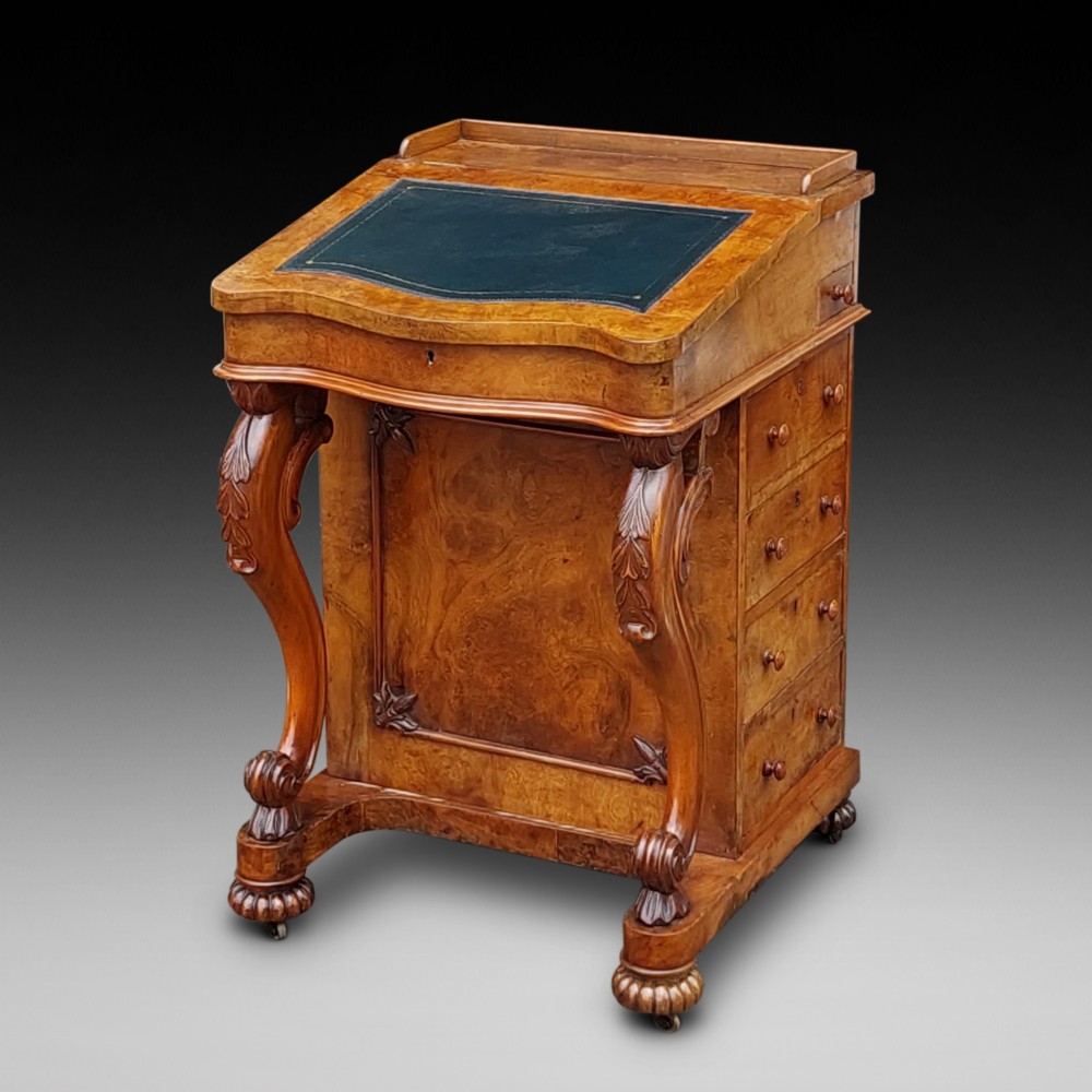 A Victorian burr walnut Davenport desk featuring a green leather sloped writing surface, carved cabriole front supports, and side drawers on castors.
