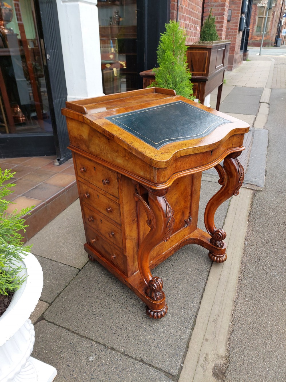 A Victorian burr walnut Davenport desk featuring a green leather sloped writing surface, carved cabriole front supports, and side drawers on castors. View IV