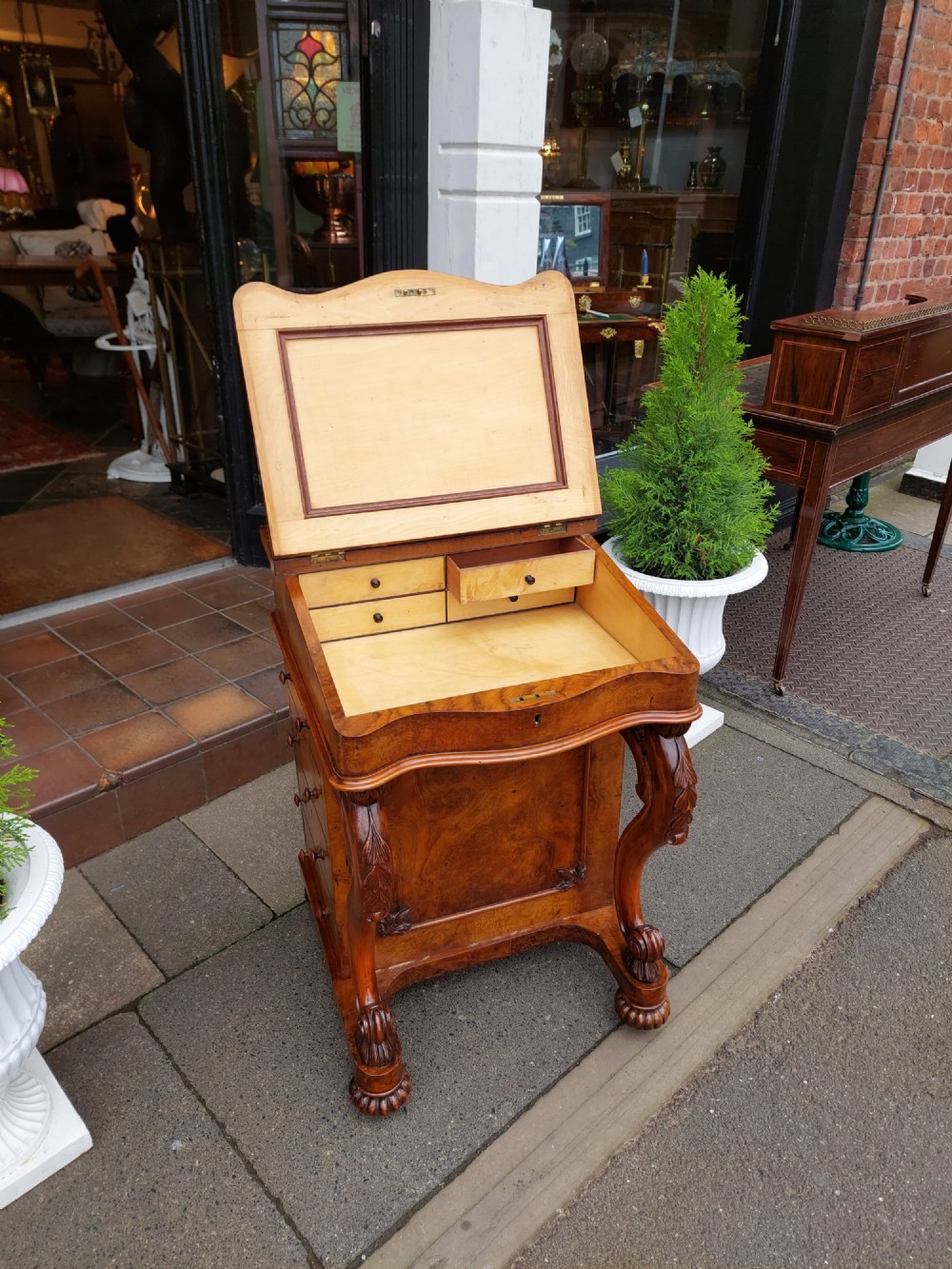 A Victorian burr walnut Davenport desk featuring a green leather sloped writing surface, carved cabriole front supports, and side drawers on castors. View V