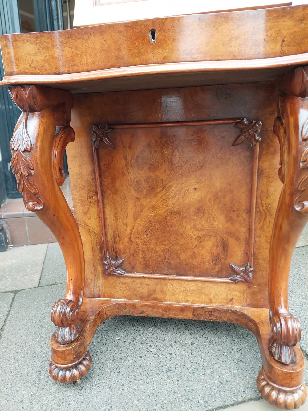 A Victorian burr walnut Davenport desk featuring a green leather sloped writing surface, carved cabriole front supports, and side drawers on castors. View VI