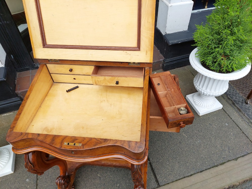 A Victorian burr walnut Davenport desk featuring a green leather sloped writing surface, carved cabriole front supports, and side drawers on castors. View VIII