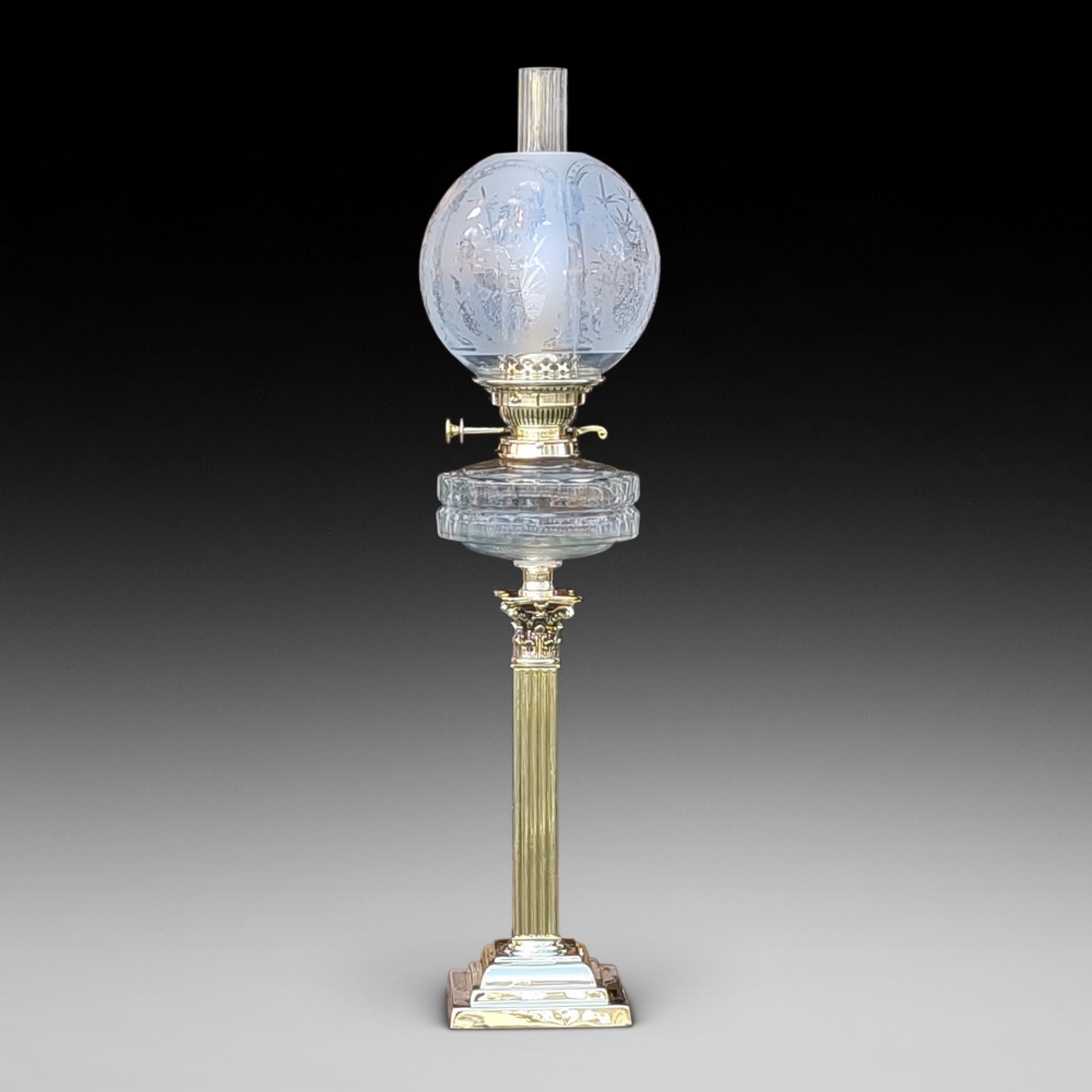 A Victorian brass oil lamp featuring a fluted Corinthian column base, a clear glass reservoir, and an etched spherical glass shade.