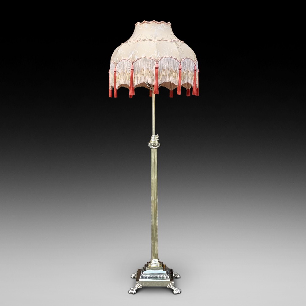 A Victorian Neoclassical brass floor lamp featuring a fluted column shaft, Corinthian capital detail, stepped base on claw feet, and a cream fringed fabric shade.