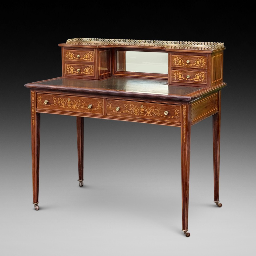Late Victorian inlaid mahogany writing desk featuring an upper mirror-backed superstructure with brass gallery, leather writing surface, floral marquetry, and tapered legs on castors.