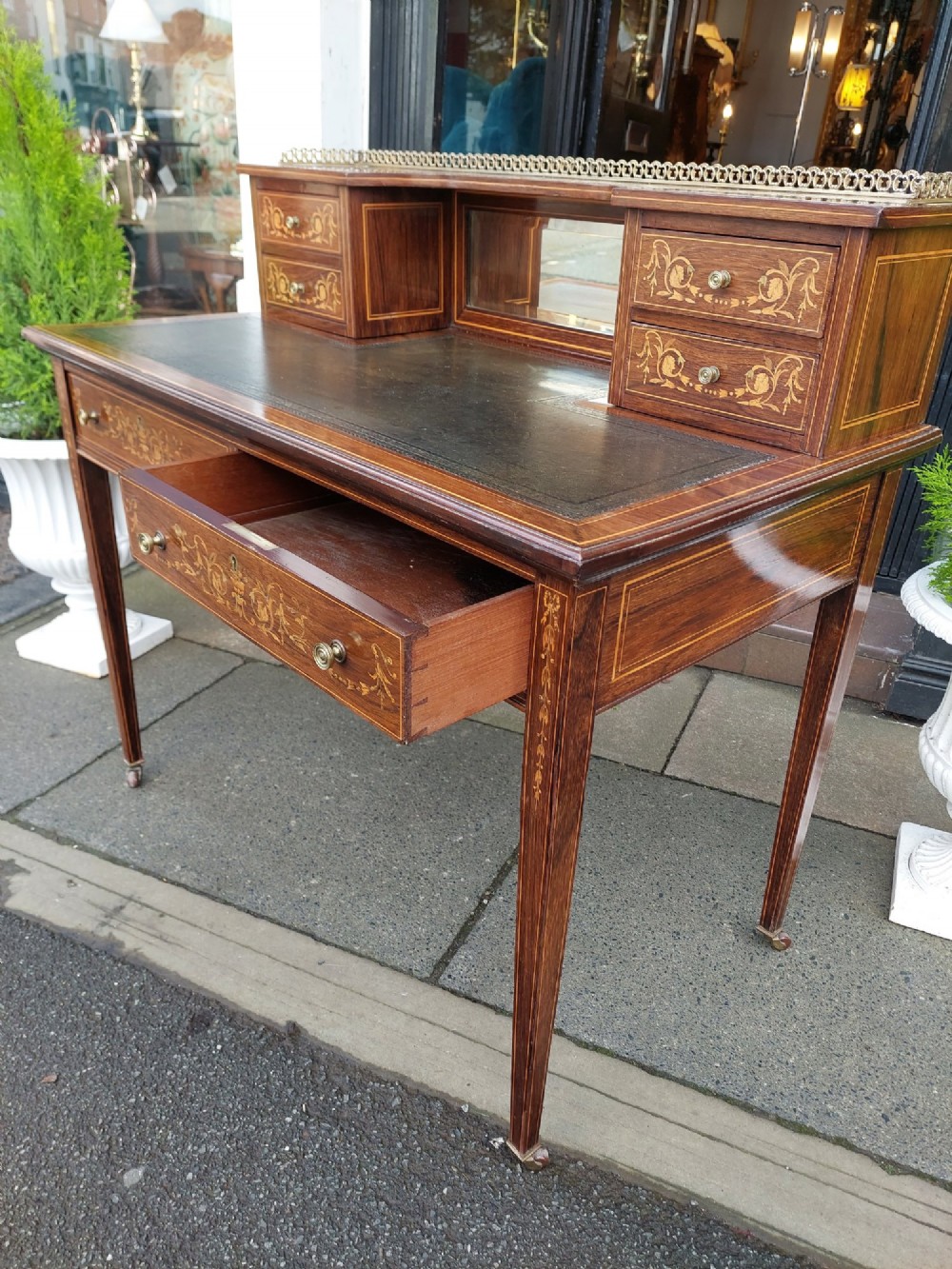 Late Victorian inlaid mahogany writing desk featuring an upper mirror-backed superstructure with brass gallery, leather writing surface, floral marquetry, and tapered legs on castors. View VIII