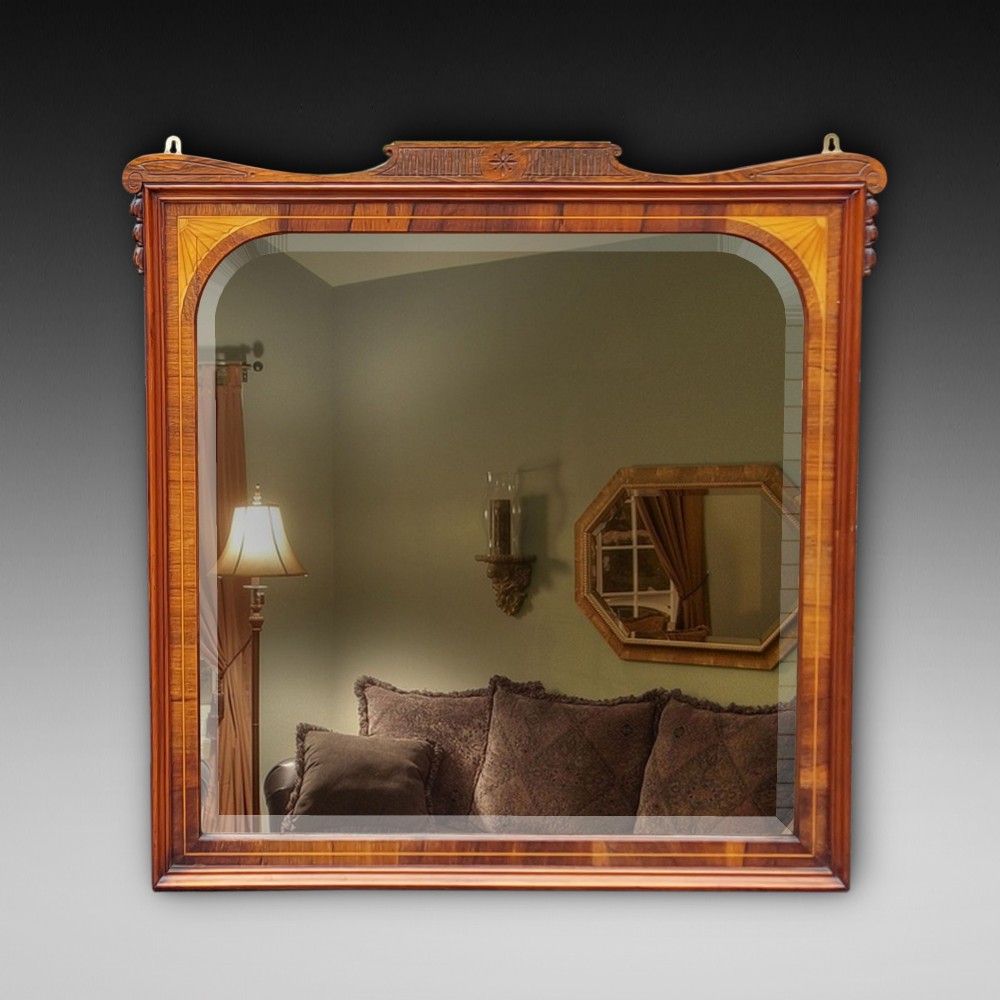 An Edwardian rosewood rectangular overmantel mirror featuring decorative marquetry inlays in the upper corners, a central carved cresting, and a bevelled glass plate.