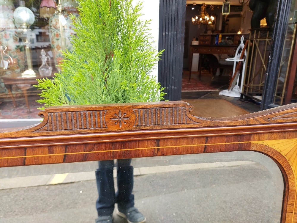 An Edwardian rosewood rectangular overmantel mirror featuring decorative marquetry inlays in the upper corners, a central carved cresting, and a bevelled glass plate. View II