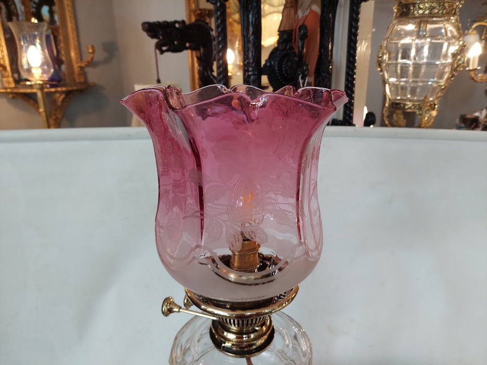 A late 19th-century brass table oil lamp featuring a reeded column, square base, clear glass reservoir, and an etched pink glass shade with a ruffled rim. View IV