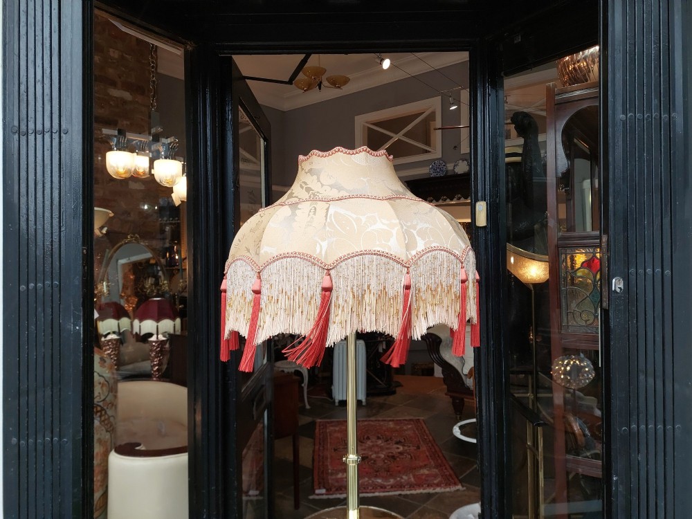 An Edwardian brass standard floor lamp featuring a scrollwork tripod base, an integrated circular tray table, and a fabric shade with fringe and tassels. View IX