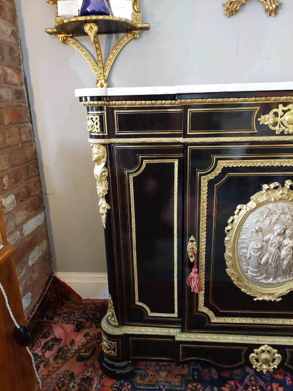 A French Napoleon III ebonised side cabinet featuring a white marble top, gold brass inlays, gilt-bronze ormolu mounts, and a central oval medallion. View V