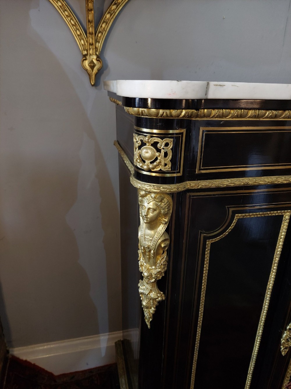 A French Napoleon III ebonised side cabinet featuring a white marble top, gold brass inlays, gilt-bronze ormolu mounts, and a central oval medallion. View VI