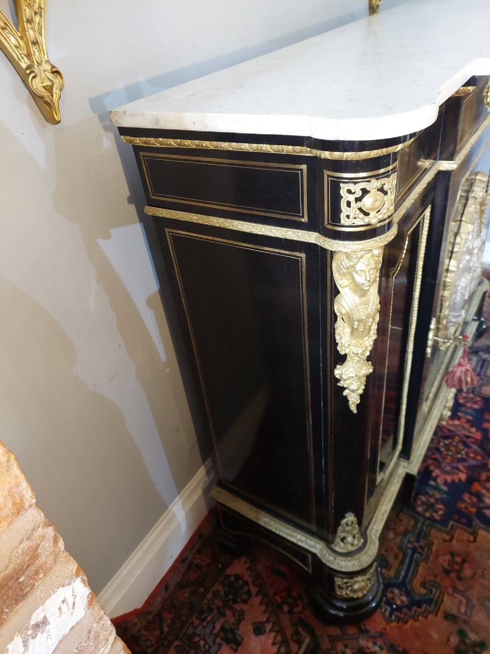 A French Napoleon III ebonised side cabinet featuring a white marble top, gold brass inlays, gilt-bronze ormolu mounts, and a central oval medallion. View VII