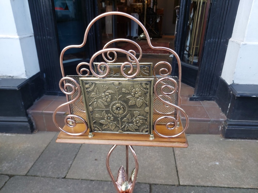 An Arts and Crafts copper and brass standing magazine rack featuring embossed floral metal panels, decorative wire scrollwork, and a tripod base with curved feet. View III