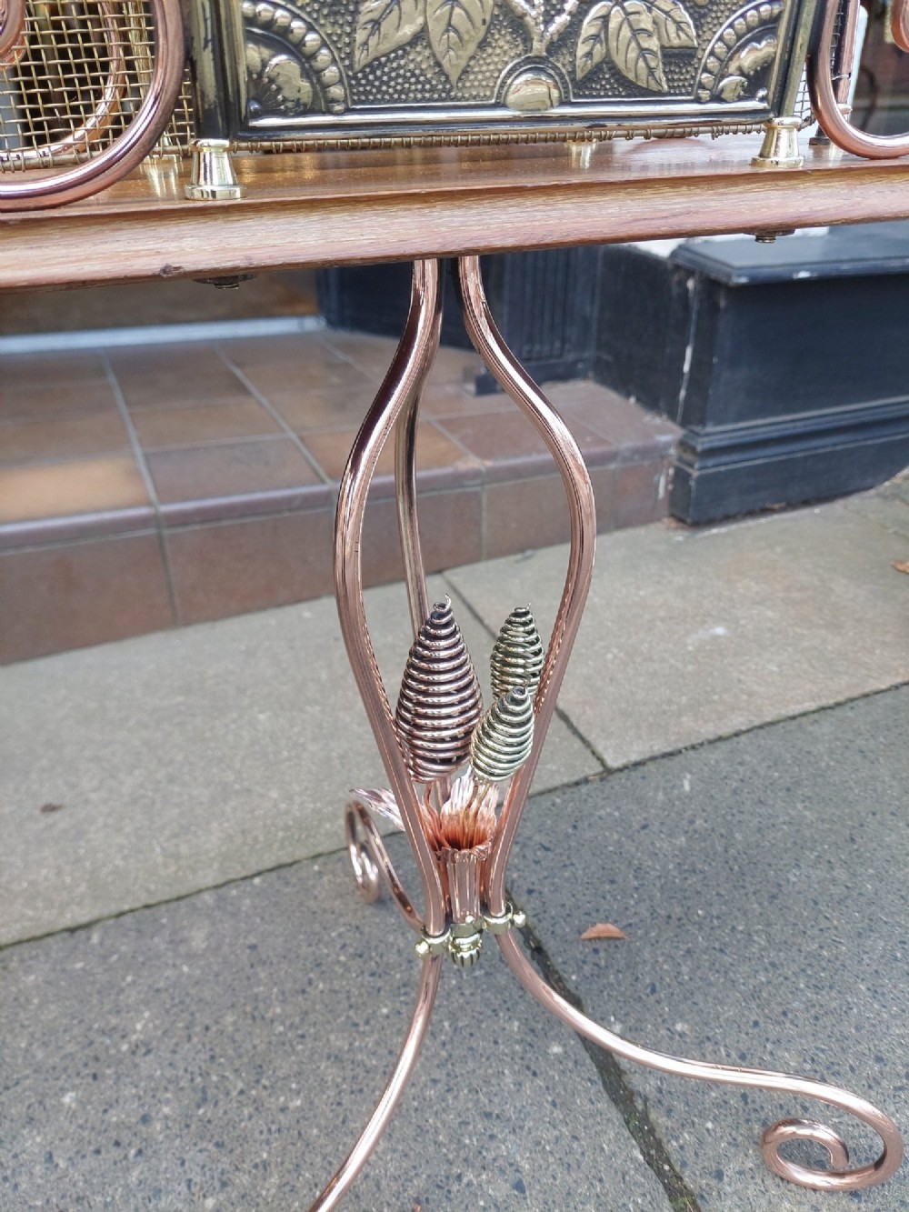 An Arts and Crafts copper and brass standing magazine rack featuring embossed floral metal panels, decorative wire scrollwork, and a tripod base with curved feet. View IV