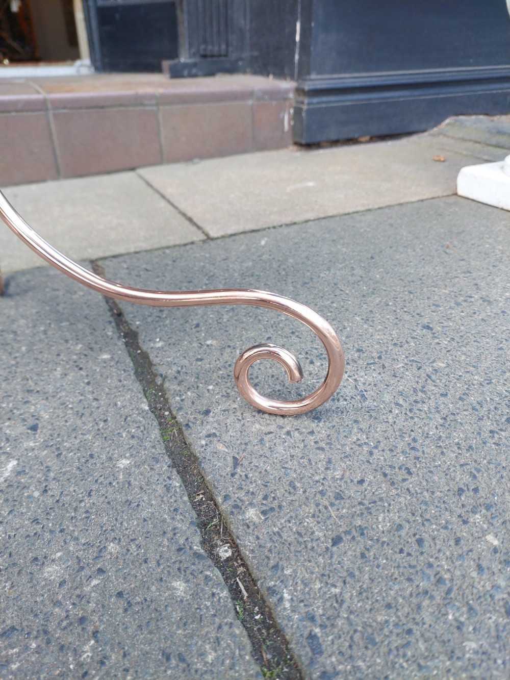 An Arts and Crafts copper and brass standing magazine rack featuring embossed floral metal panels, decorative wire scrollwork, and a tripod base with curved feet. View VI