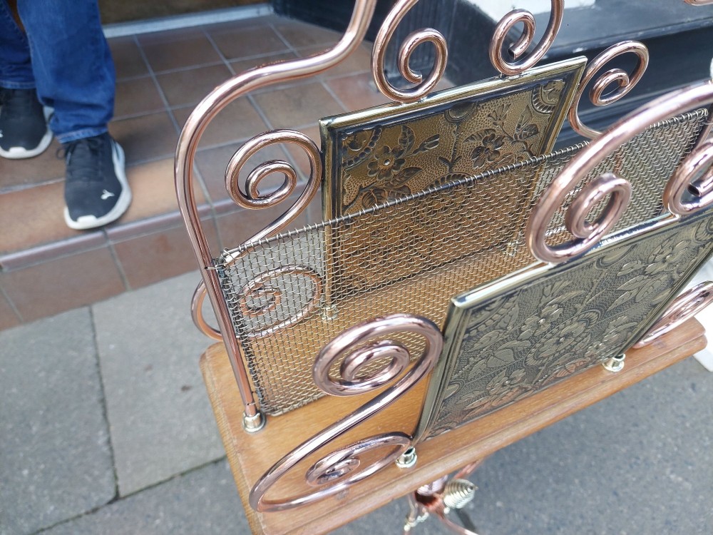 An Arts and Crafts copper and brass standing magazine rack featuring embossed floral metal panels, decorative wire scrollwork, and a tripod base with curved feet. View VII